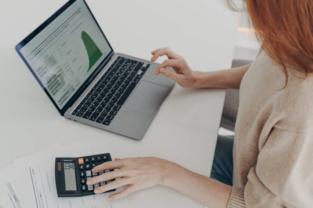 A woman reviewing debt consolidation options on a laptop and calculating monthly payments.